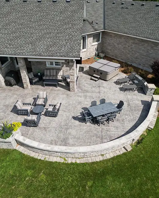 Rounded concrete patio area with two sets of tables and chairs, two pool chairs and a hot tub